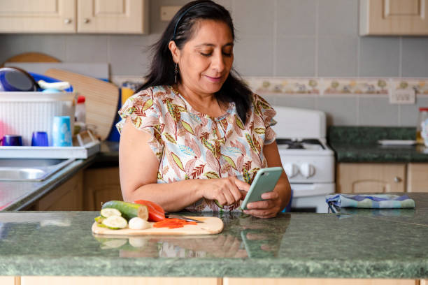 Mature woman preparing healthy and organic salad while checking her cell phone-housewife cooking while she looks at a phone